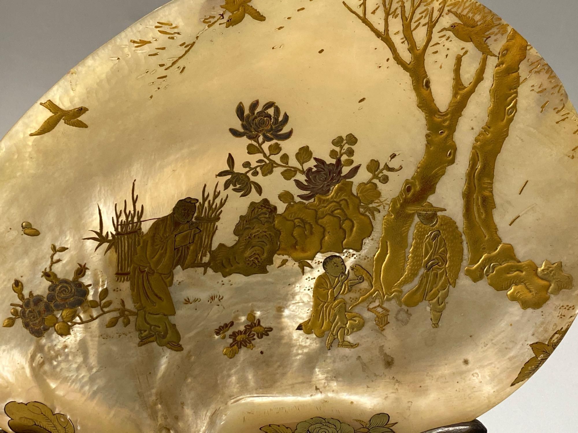 A pair of Chinese mother opearl dishes, gilt lacquered with figures and birds in landscapes, on carved hardwood stand, 26cm